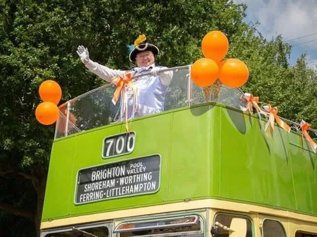Bob Smytherman waving from the open top deck of a vintage Southdown bus during a local parade, its blind reading Shoreham, Worthing, Ferring and Littlehampton.